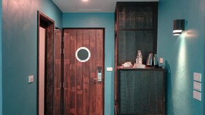 Een gang met een houten deur, een wandlamp en een plank met een waterkoker en andere spullen.