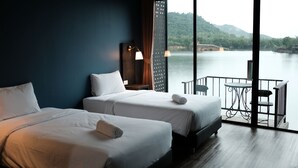 Een hotelkamer met twee bedden, een balkon met een tafel en stoelen, en uitzicht op water en heuvels.