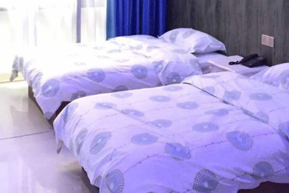 Habitación de hotel con dos camas, una pared de madera y una ventana con cortinas azules.