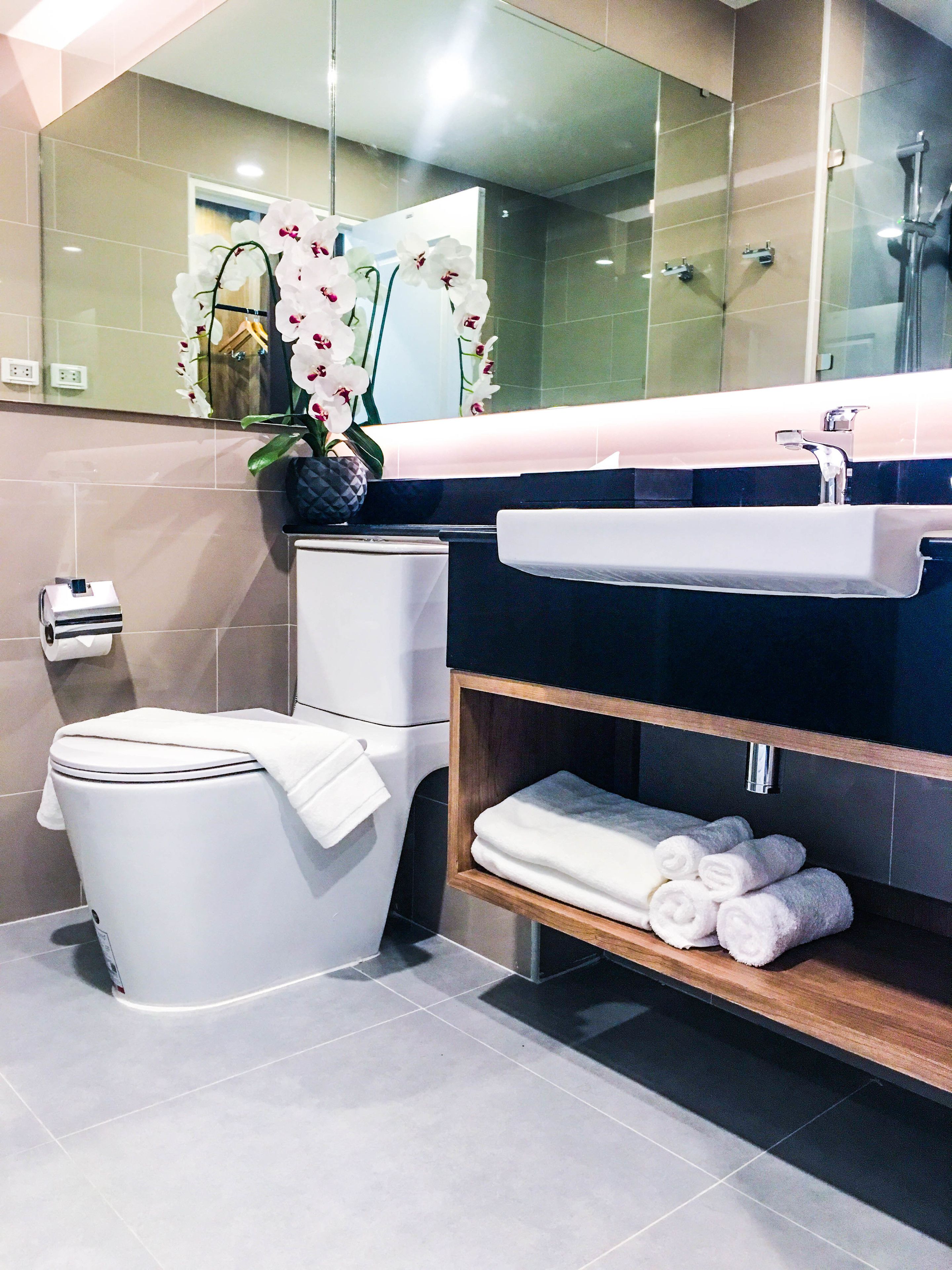 Une salle de bain moderne équipée de toilettes, d’un lavabo et d’une étagère où sont pliées des serviettes.