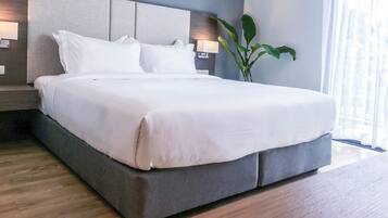 Una habitación de hotel moderna con una cama grande, cabecero, lámpara de noche y una planta en maceta.
