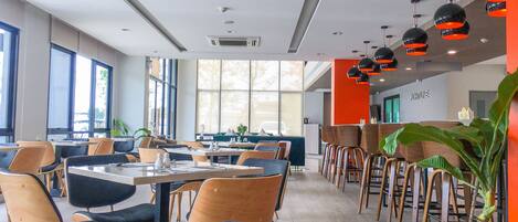 A modern restaurant with a mix of wooden and upholstered chairs, large windows, and a bright interior.