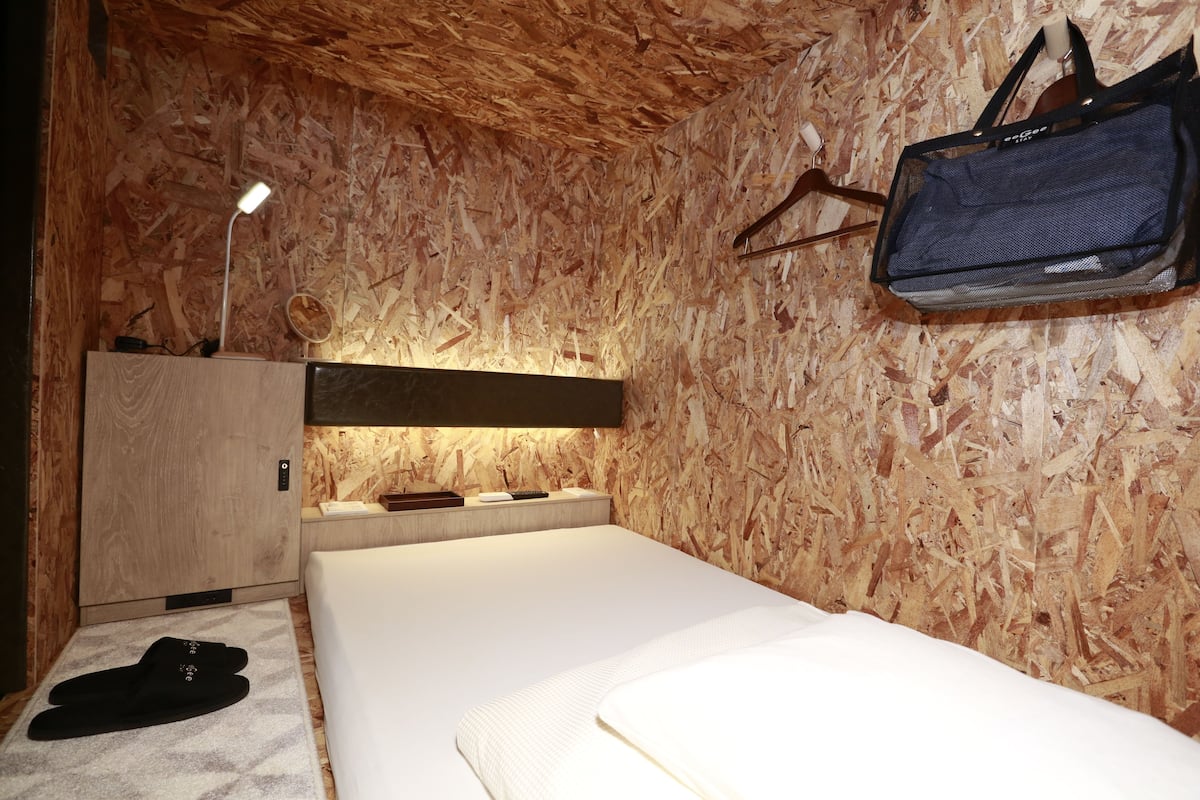 A room with a bed, a desk, a lamp, and a hanging bag.