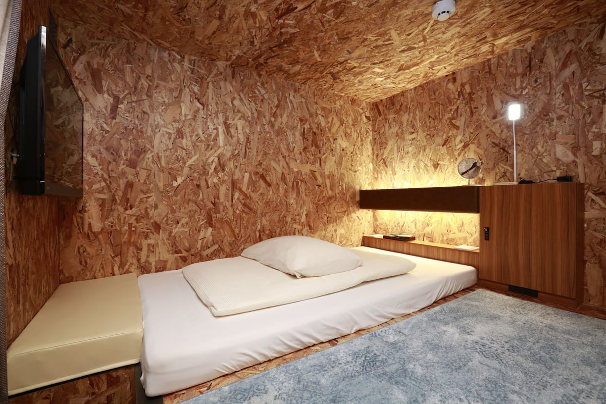 A bedroom with a bed, a nightstand, a lamp, and a wooden ceiling.