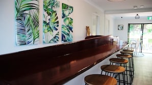 A bar area with a long counter and multiple stools. There are large abstract paintings on the wall. - Yeppoon Beachhouse - Hostel (Yeppoon)