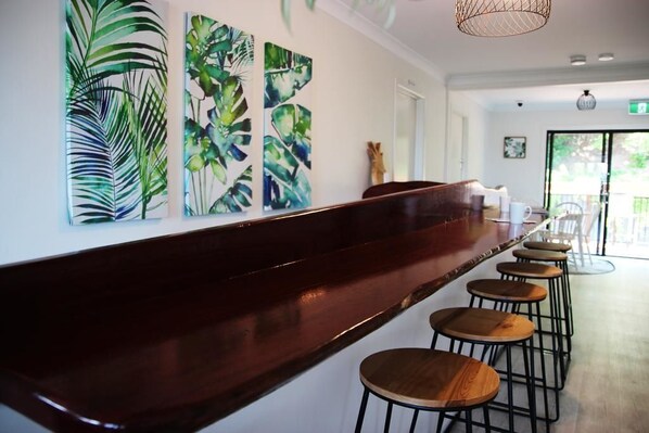A bar area with a long counter and multiple stools. There are large abstract paintings on the wall. - Yeppoon Beachhouse - Hostel (Yeppoon)