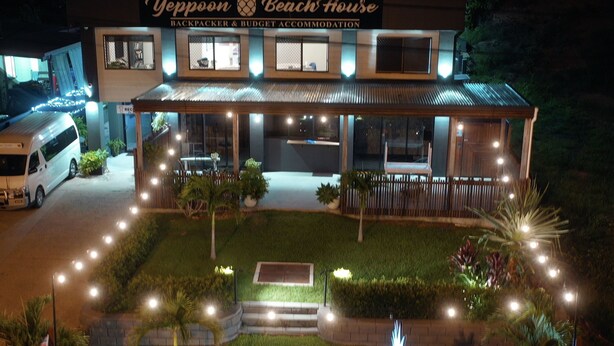 A two-story building with a sign reading "Yeppoon Beach House Backpacker & Budget Accommodation". There are steps leading to the entrance, a small garden with plants, and a fence around the property. - Yeppoon Beachhouse - Hostel (Yeppoon)