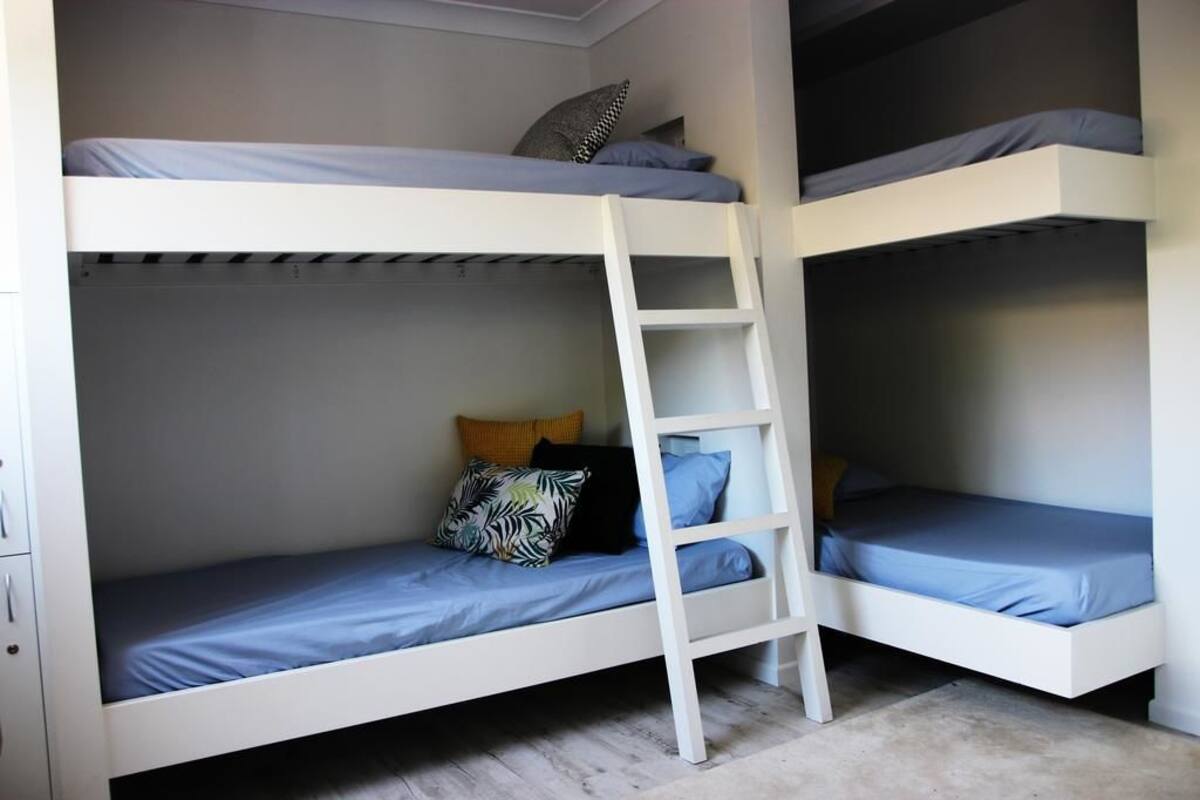 Une chambre avec un lit superposé, une échelle, deux lits et un petit placard.