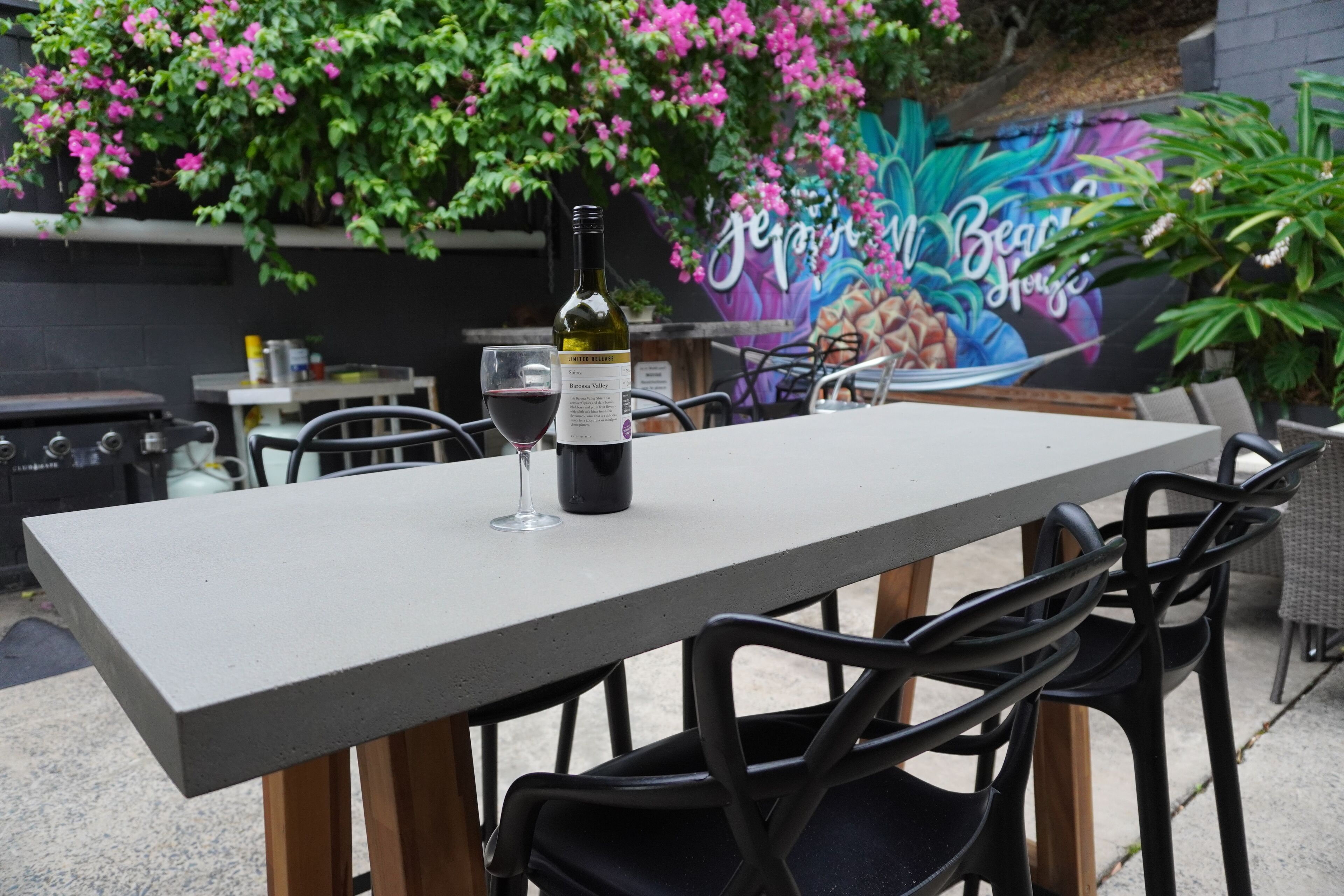 An outdoor dining area with a table, chairs, a bottle of wine, and a glass.