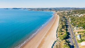 An aerial view of a coastal area with a long sandy beach, a road parallel to the shore, and a residential area with houses and greenery. - Yeppoon Beachhouse - Hostel (Yeppoon)