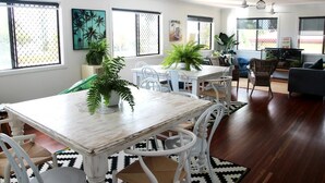 A dining area with a white table and chairs, surrounded by potted plants and artwork. - Yeppoon Beachhouse - Hostel (Yeppoon)
