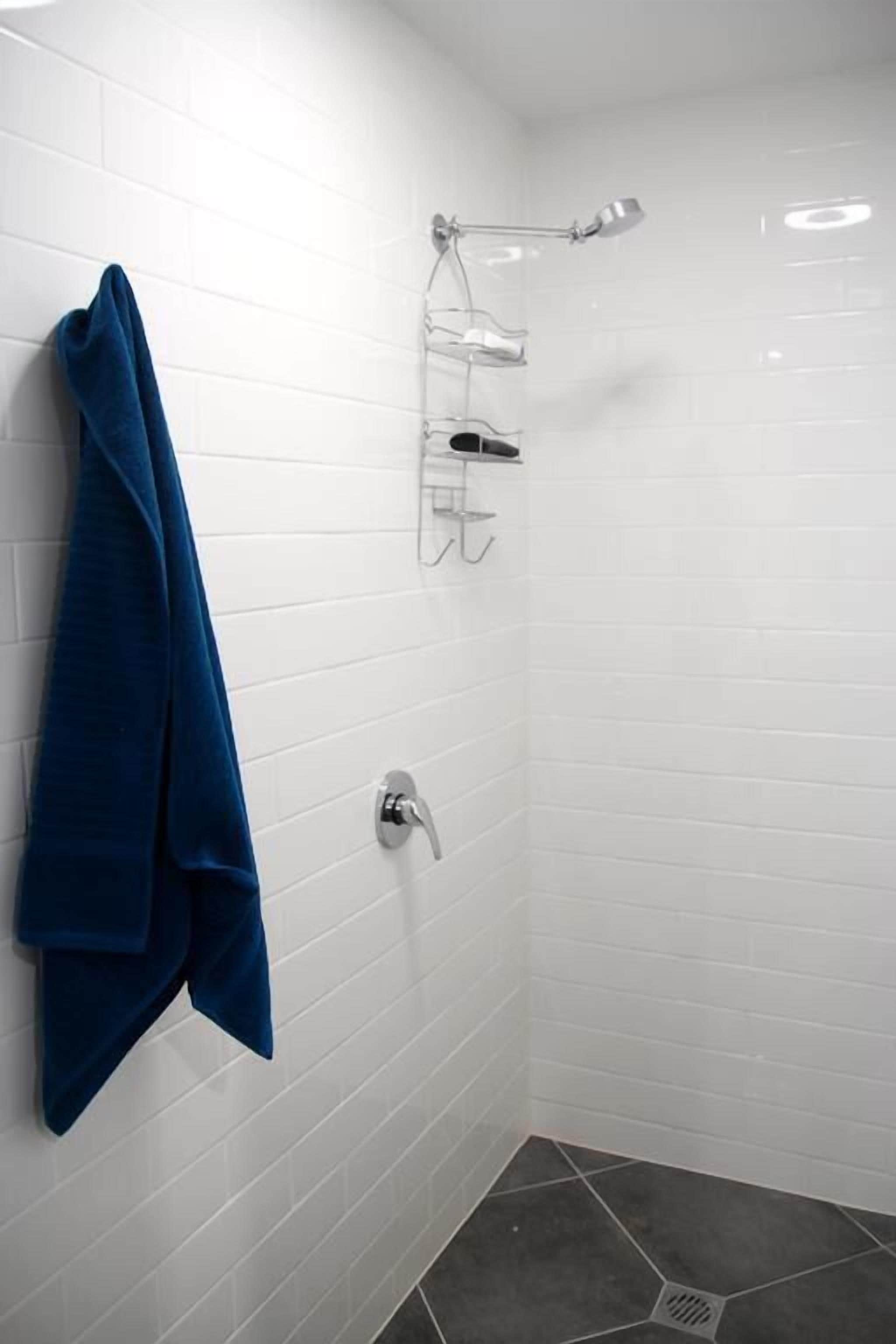 Een kleine, betegelde doucheruimte met witte tegels, een blauwe handdoek aan de muur, een douchekop en een handdouche.