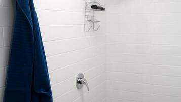 Een kleine, betegelde doucheruimte met witte tegels, een blauwe handdoek aan de muur, een douchekop en een handdouche.