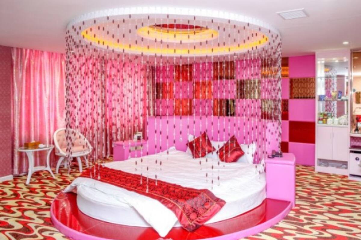 Uma cama redonda com colcha branca e vermelha, cortinas cor-de-rosa e parede rosa com padrão.