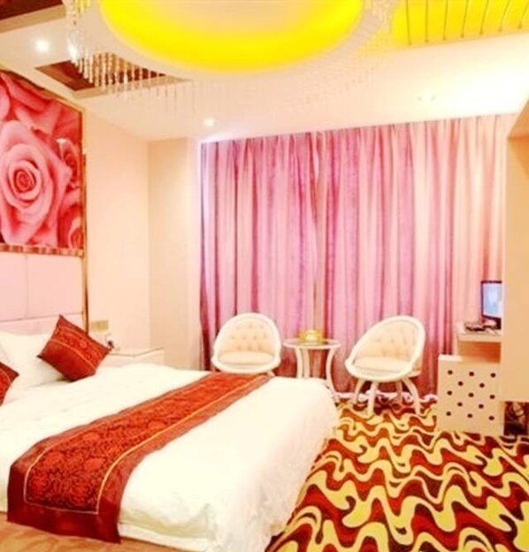 A hotel room with a bed, a red and yellow patterned carpet, a pink curtain, and two white chairs.