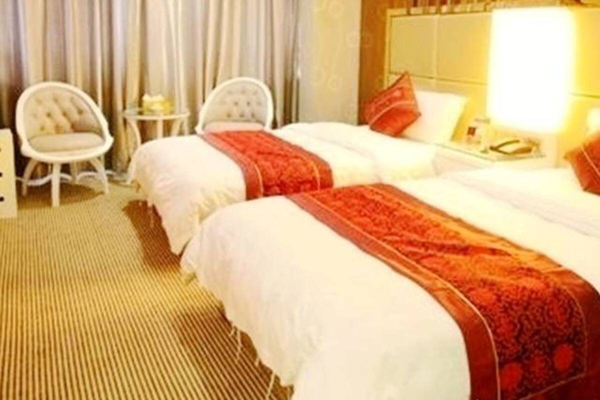 Quarto de hotel com duas camas, área de estar com uma cadeira e uma pequena mesa, e um espelho grande sobre a cama.
