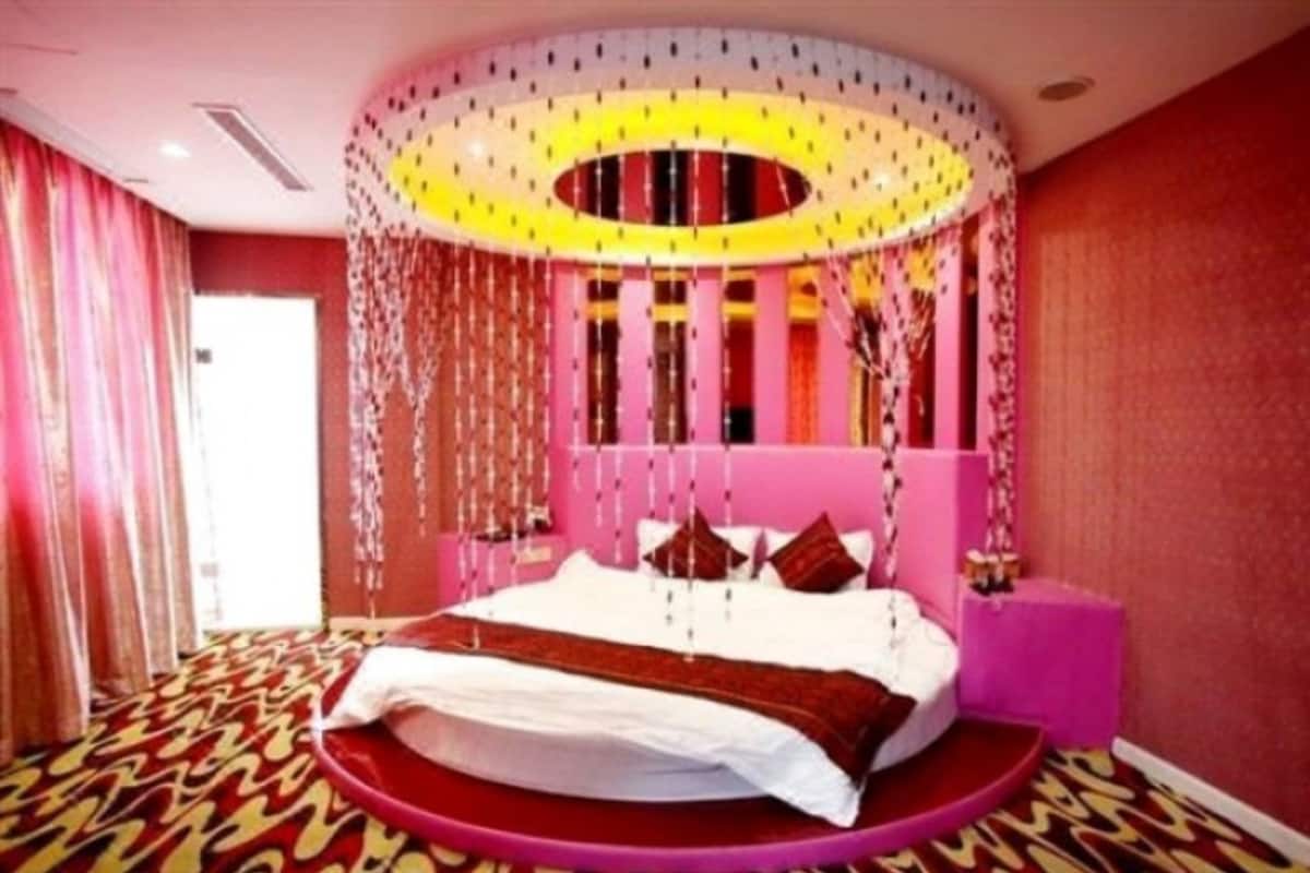 Cama redonda com cabeceira rosa, tapete estampado e teto com decorações pendentes.
