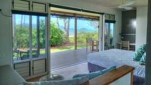 A bedroom with a large sliding glass door leading to a balcony, a bed, a chair, and a small table. - The Bungalows (Wongaling Beach)
