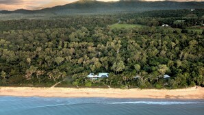 An aerial view of a coastal area with dense forest, a beach, and a few buildings. - The Bungalows (Wongaling Beach)