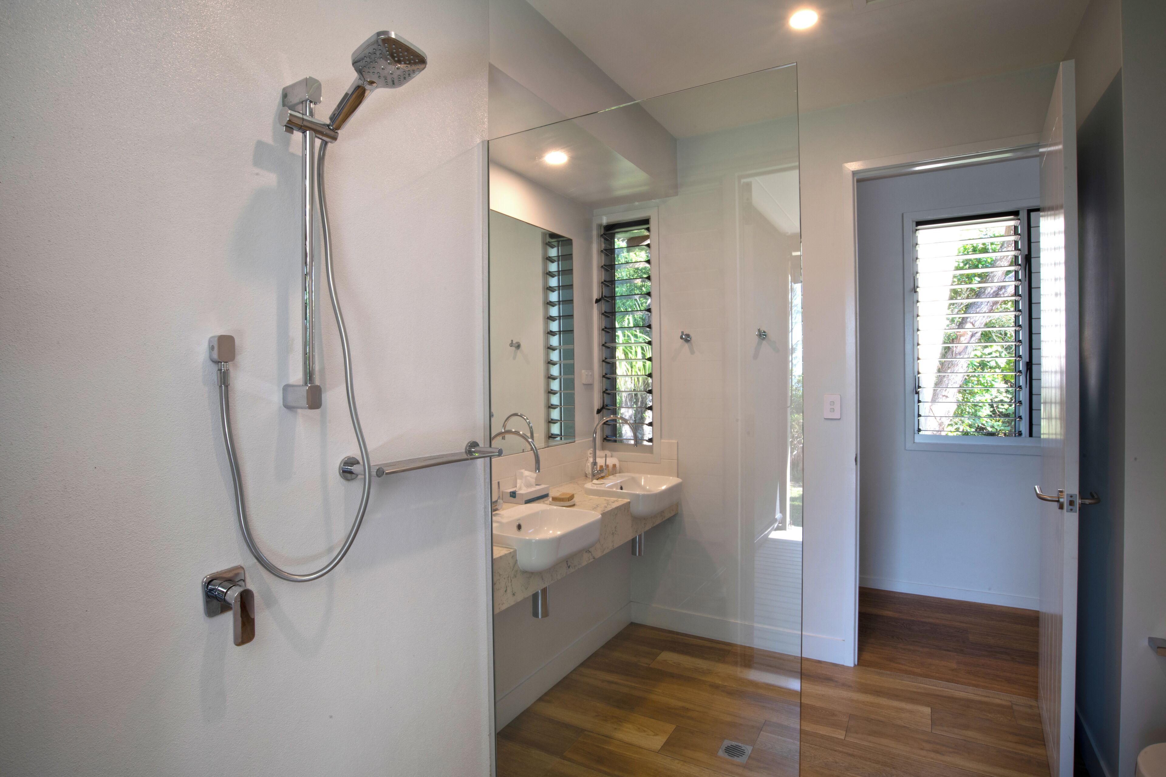 A modern bathroom with a shower, two sinks, and a large mirror.