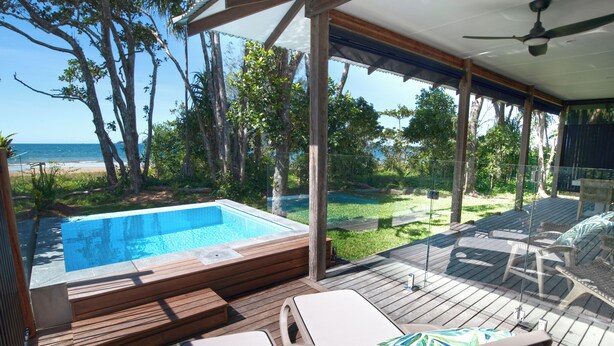 A poolside area with a hot tub, lounge chairs, and a view of the beach. - The Bungalows (Wongaling Beach)