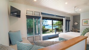 A modern bedroom with a large bed, a wooden bench, and a view of the outdoors. - The Bungalows (Wongaling Beach)