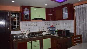 A kitchen with wooden cabinets, a gas stove, and a dining area with a table and chairs. - Golden heaven homestay (Kathmandu)