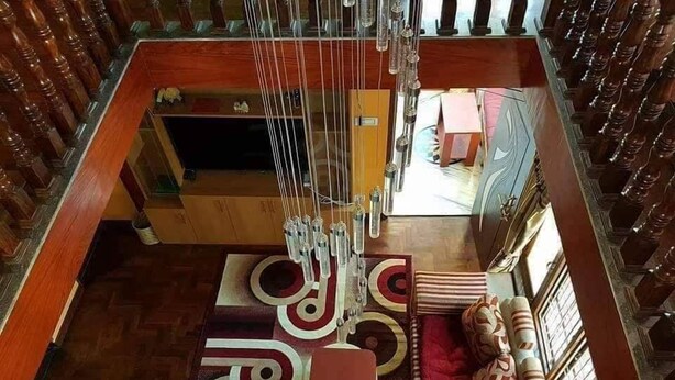 A room with a wooden floor, a patterned rug, a red upholstered sofa, and a decorative wall hanging. - Golden heaven homestay (Kathmandu)