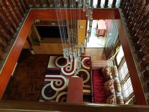 A room with a wooden floor, a patterned rug, a red upholstered sofa, and a decorative wall hanging. - Golden heaven homestay (Kathmandu)