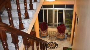 A staircase with wooden balusters leading to a balcony with wicker furniture and a view of the outside. - Golden heaven homestay (Kathmandu)