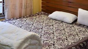 A bedroom with a wooden headboard, a patterned bedspread, a white pillow, and a ceiling fan with green lighting. - Golden heaven homestay (Kathmandu)