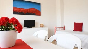 Habitació d'hotel amb un llit, una taula de treball amb un ordinador, una televisió, un vas amb una flor vermella i un quadre a la paret.
