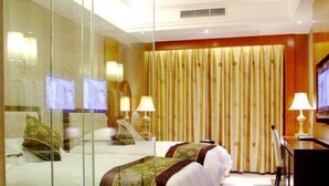 Habitació d'hotel amb un separador de vidre, dos llits amb estores estampades, una taula de treball i un televisor.