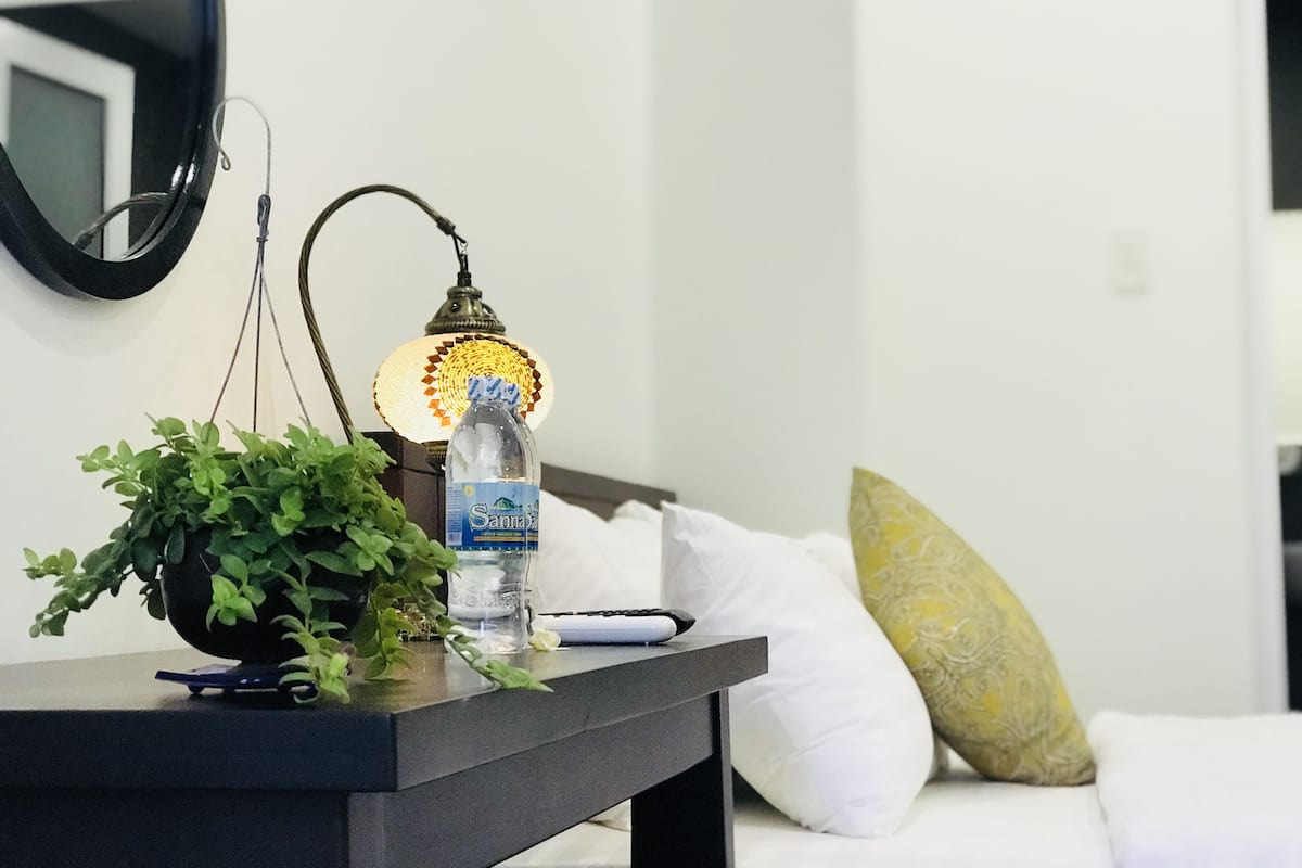 Une chambre avec un lit, une table de chevet avec une lampe, une bouteille d’eau et une plante en pot.