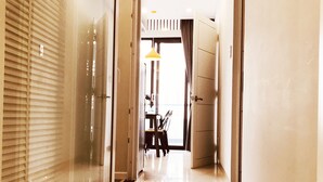 Un couloir d’hôtel avec un sol brillant, un coin repas avec une table et des chaises, et une grande fenêtre avec des stores.
