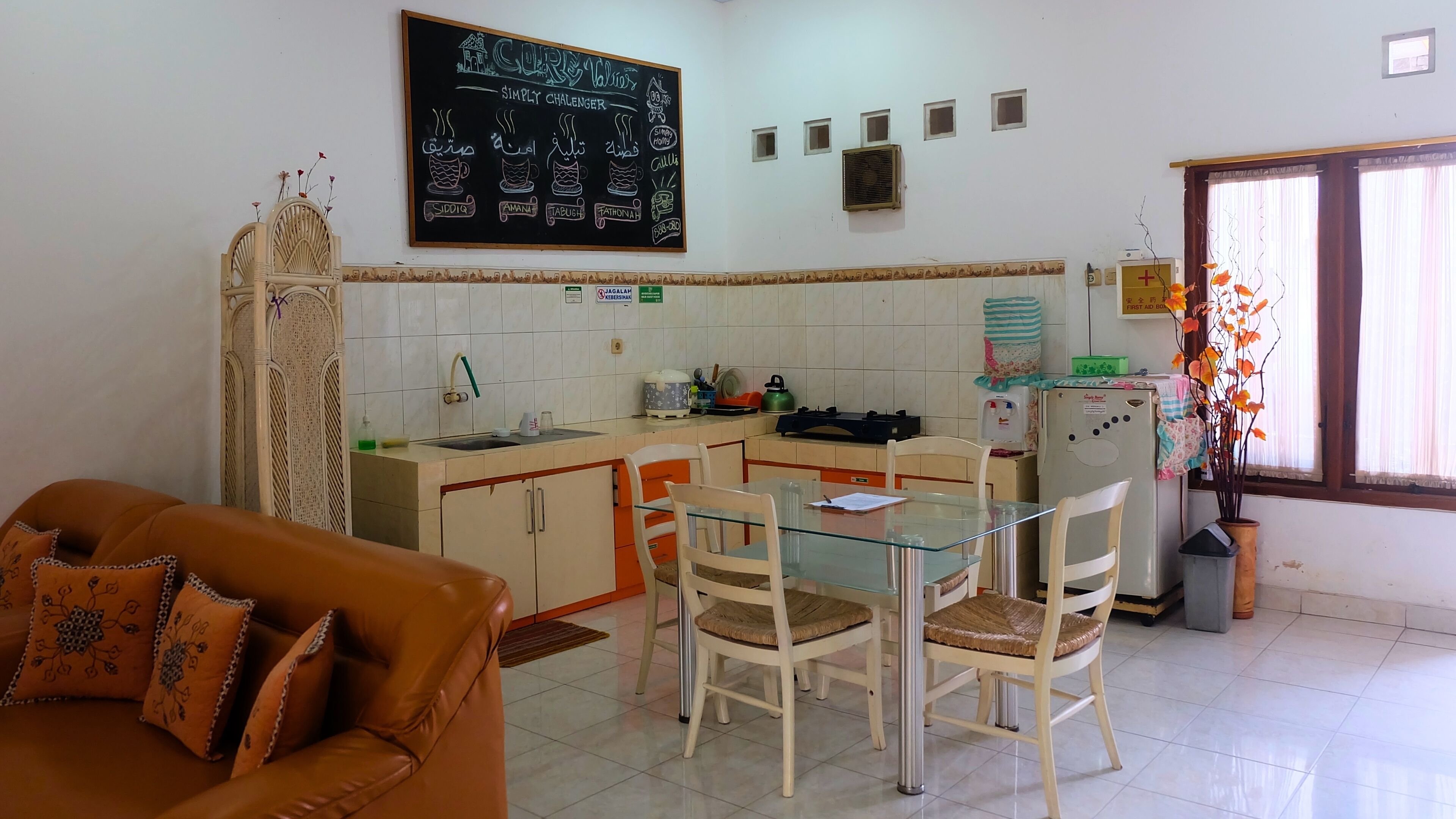 A compact living space with a kitchenette, a dining area with a glass table, and a sofa with patterned cushions.