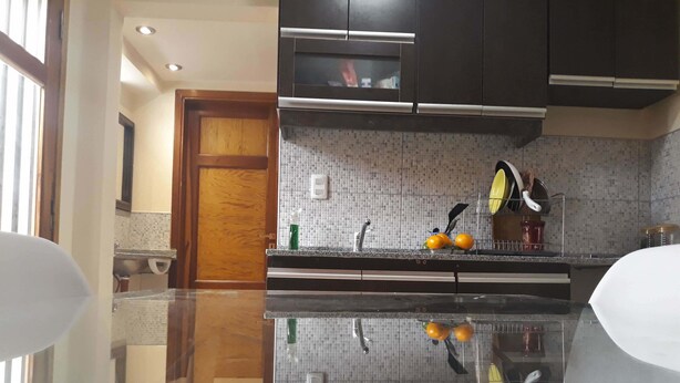 A modern kitchen with dark cabinets, a tiled backsplash, and a reflective countertop. - Drastuh Alojamientos Temporarios (Córdoba)