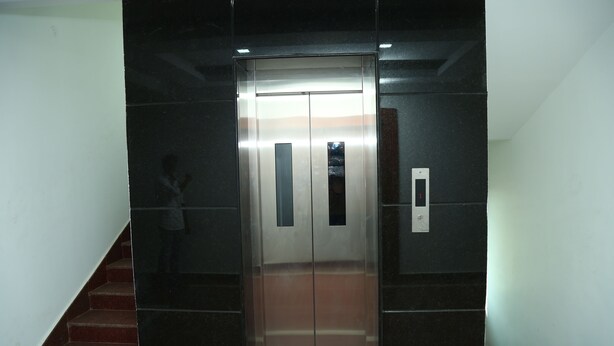Un ascensor con acabado metálico, pantalla digital y panel de control en la pared.
