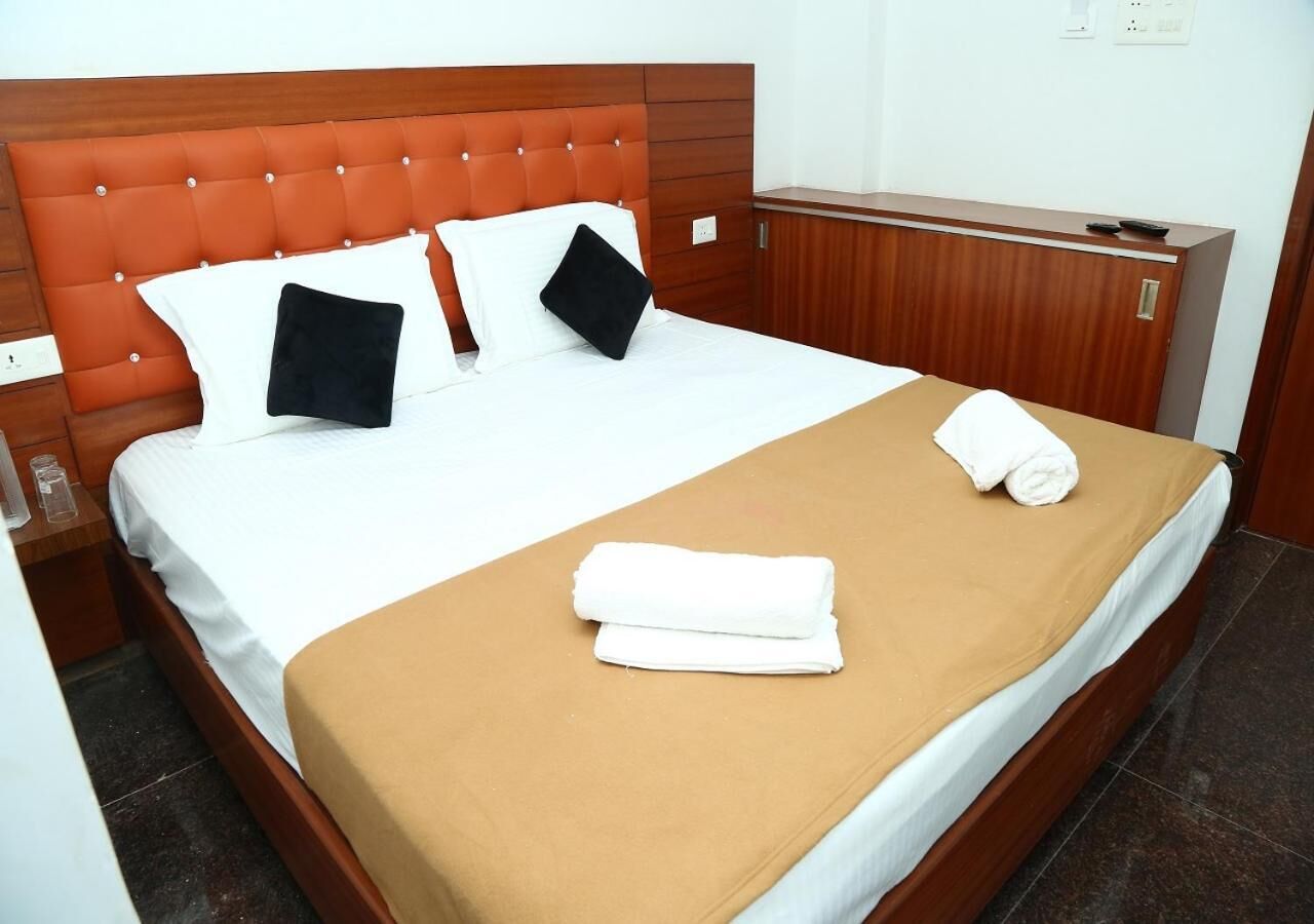A hotel room with a bed, a wooden headboard, a wooden nightstand, and a wooden dresser.