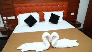Habitación de hotel con cama, dos almohadas, mesita de noche, control remoto y una escultura de toalla en la cama.