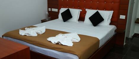 Une chambre d’hôtel avec un grand lit, une tête de lit marron, du linge de lit blanc et deux oreillers noirs.