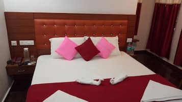 Una habitación de hotel con una cama grande, ropa de cama roja y blanca, un cabecero de madera y una mesita de noche con un teléfono, controles remotos y una botella de agua.