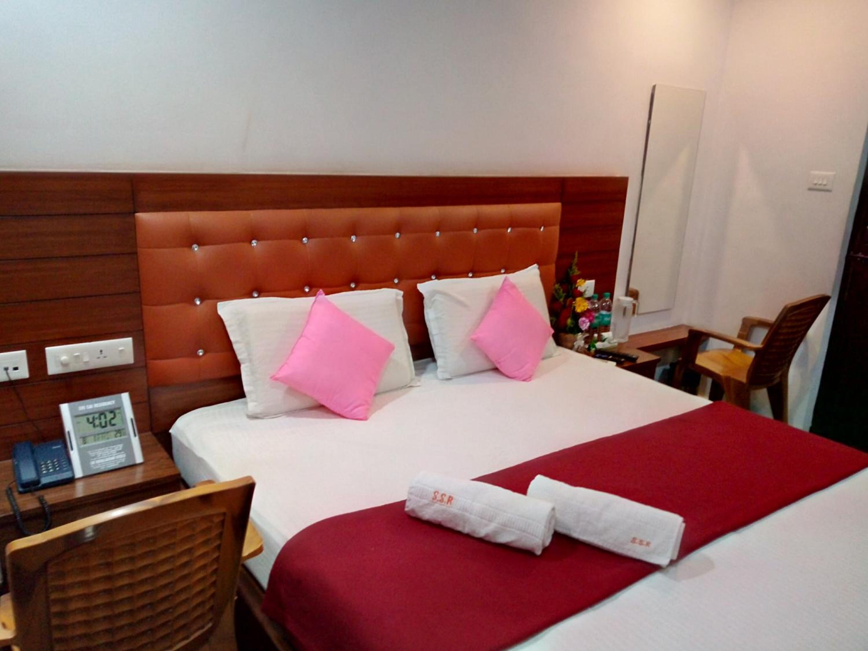 A hotel room with a large bed, a wooden headboard, a desk with a telephone, and a chair.
