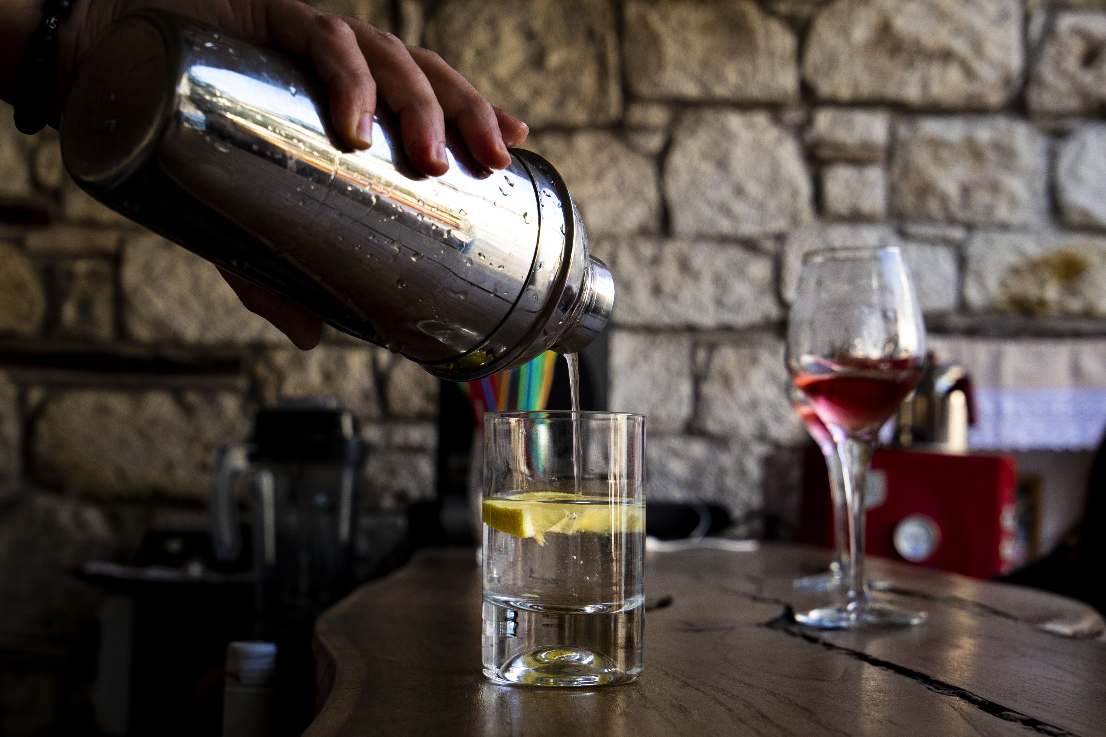 A hand pouring a drink from a shaker into a glass with a lemon slice.