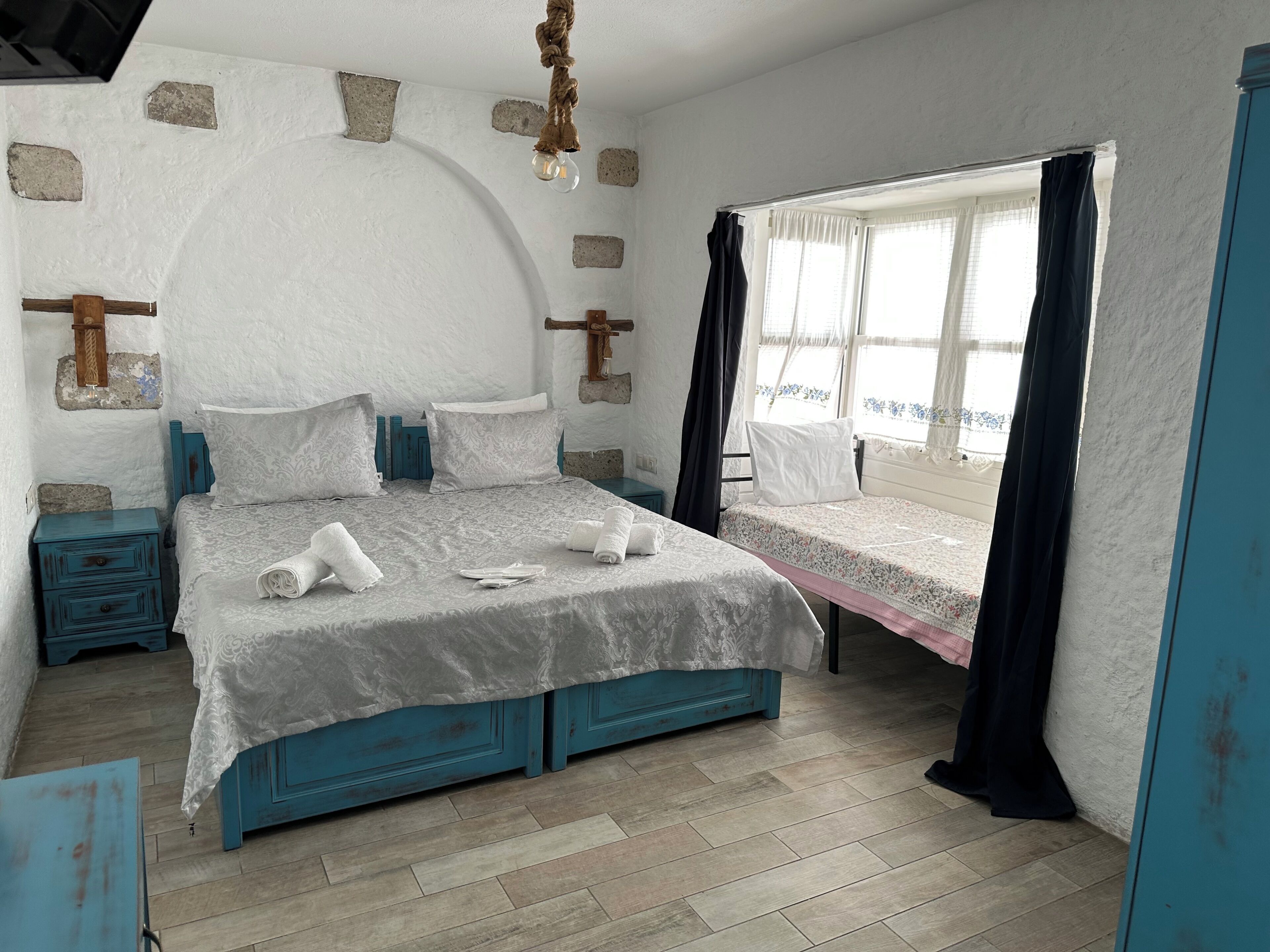 A bedroom with a bed, bedside tables, a window with curtains, and a wall with exposed bricks.
