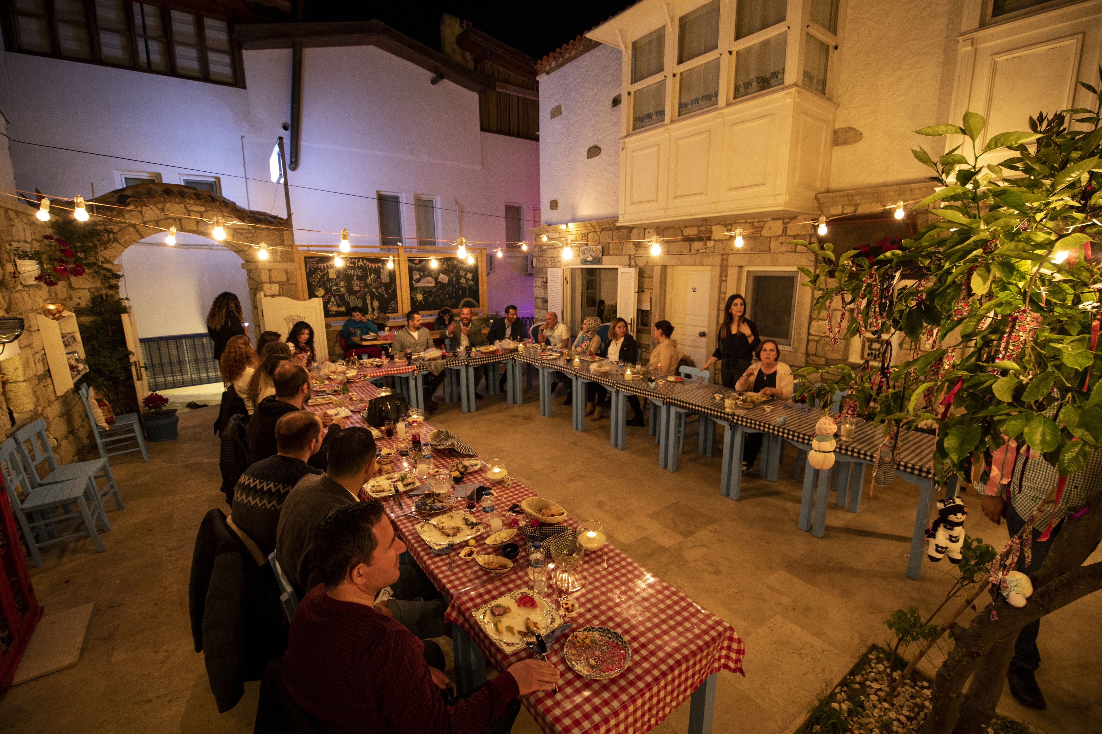 A dining area with long tables set for a meal, surrounded by stone walls and a rustic archway.