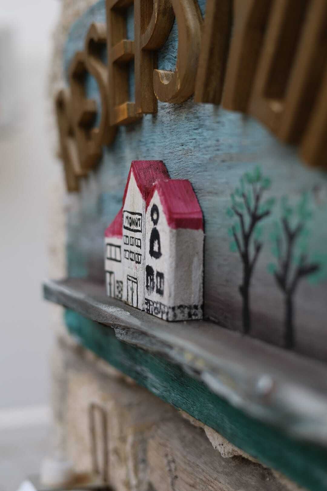 Un modelo de casa en miniatura con techo rojo y un icono de persona, sobre un estante con base verde.