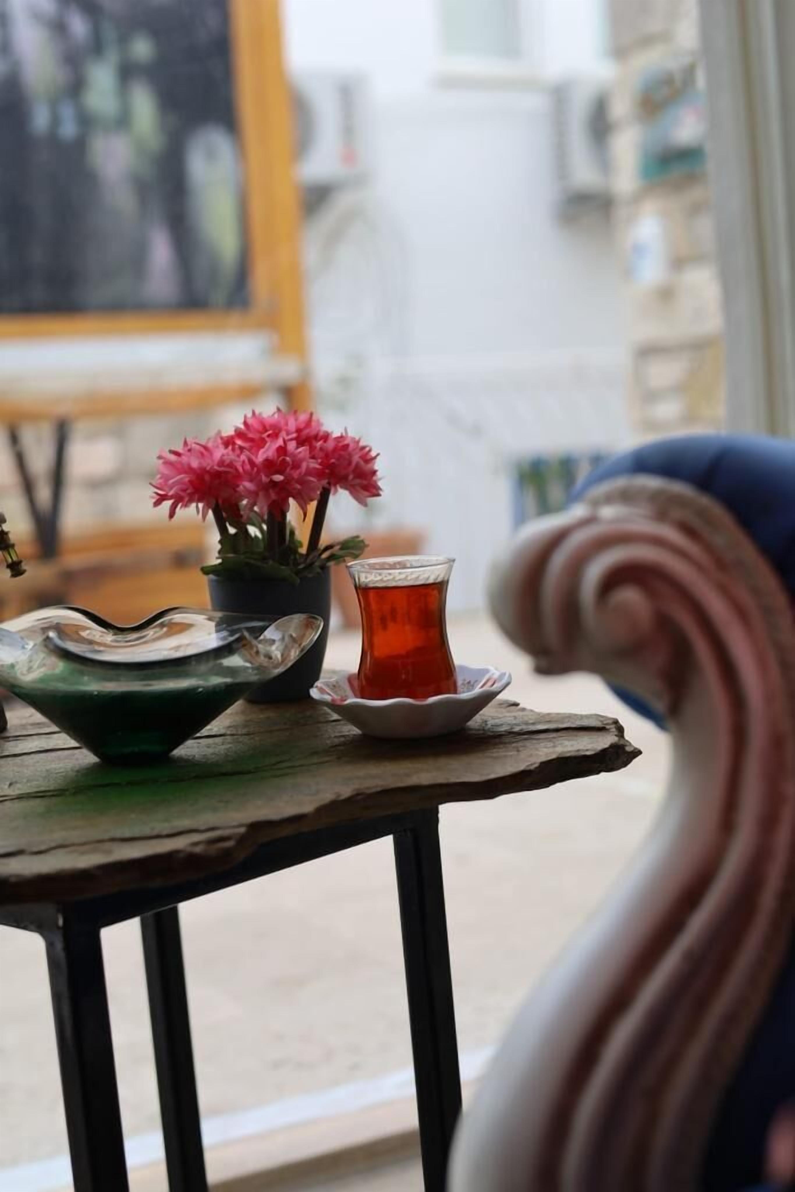 A table with a glass bowl, a green bowl, a glass of tea, and a potted plant with pink flowers.