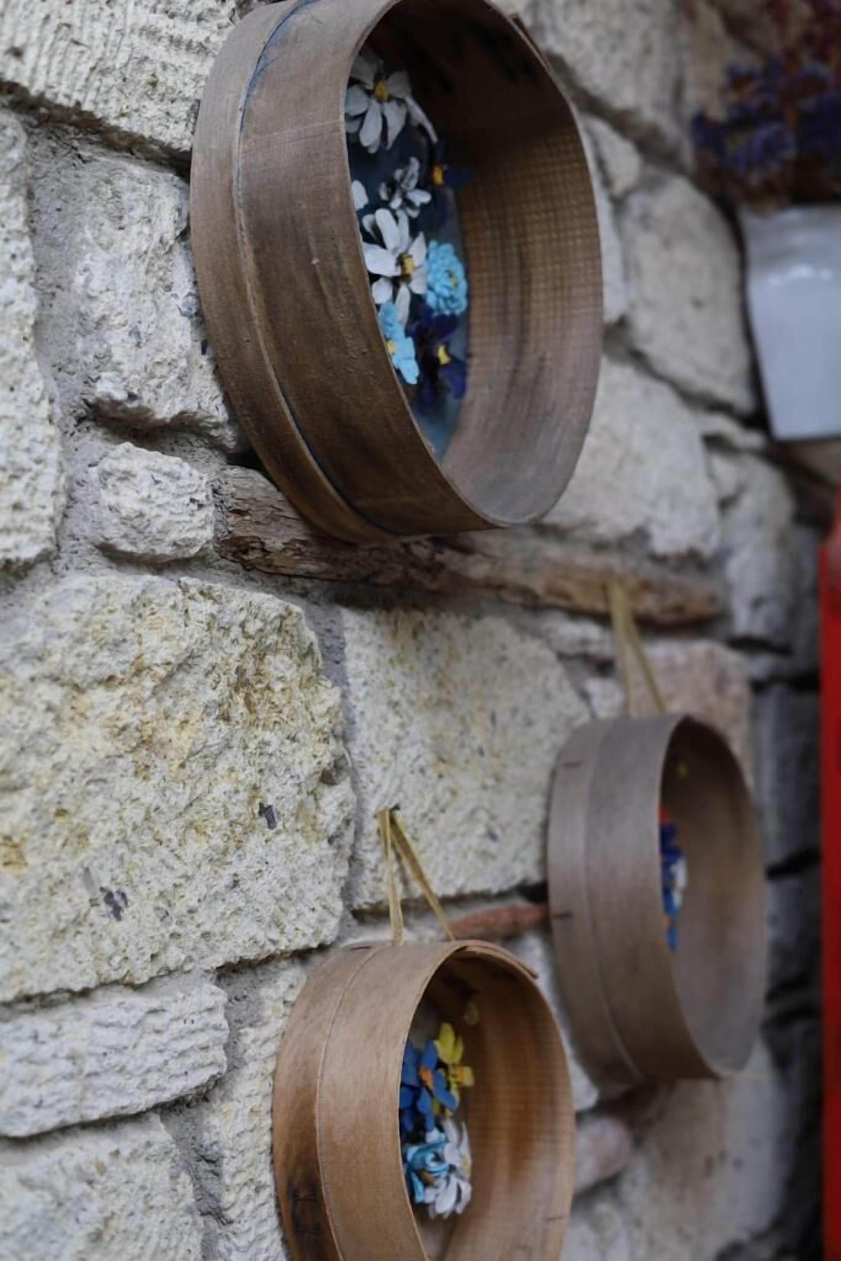 Tre fioriere in legno con fiori davanti a un muro in pietra.