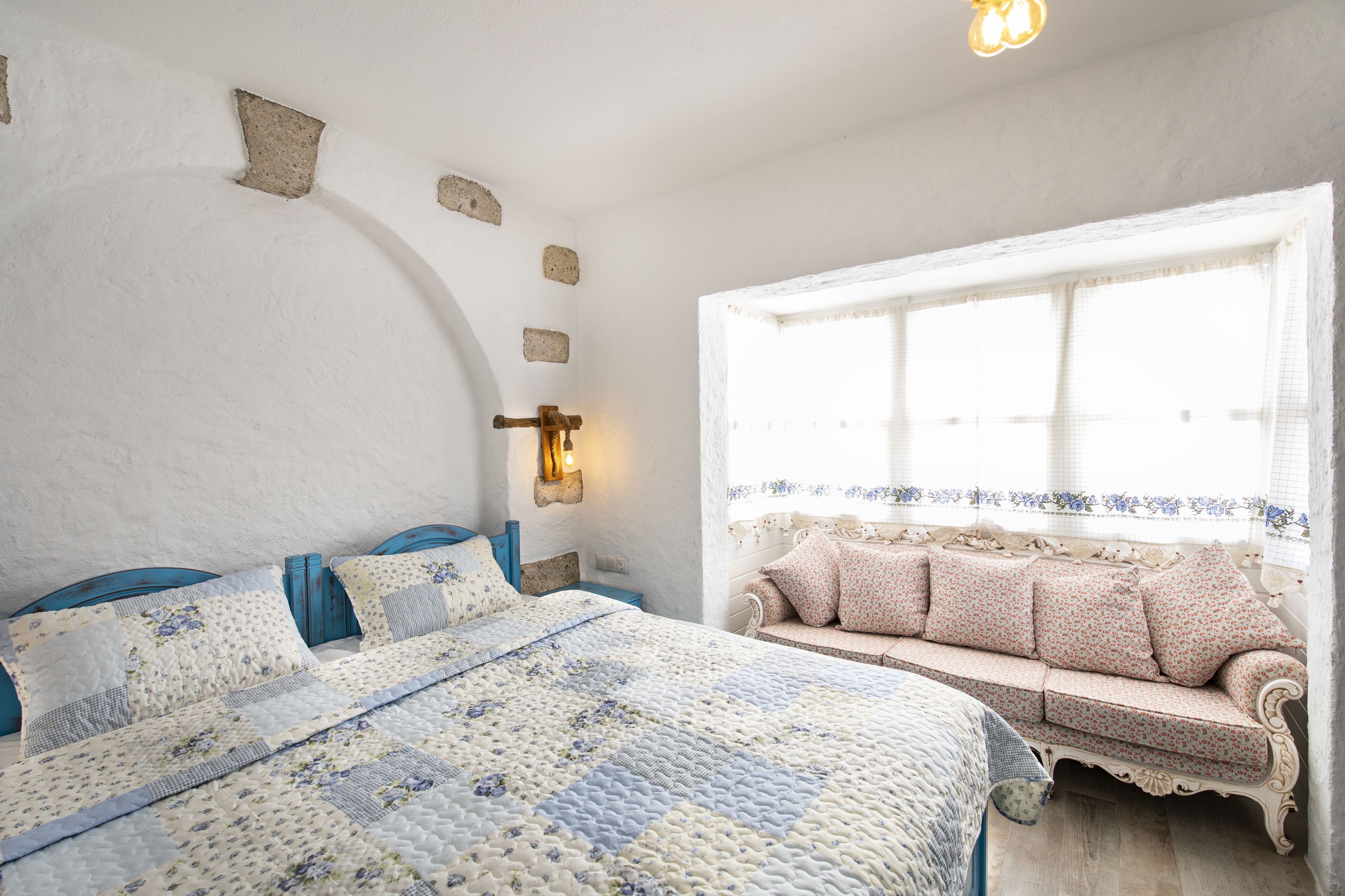 Ein Schlafzimmer mit einem Bett, einer Couch, einer Wandleuchte und einem Fenster mit Vorhängen.